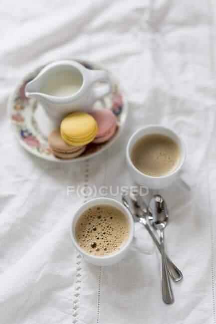 Дві чашки кави з молочним глечиком і макаронами. — стокове фото