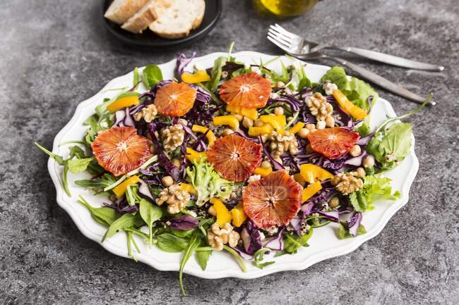 Um prato de salada com quinoa, grão de bico, pimentão amarelo, nozes, repolho vermelho e laranja sangue — Fotografia de Stock