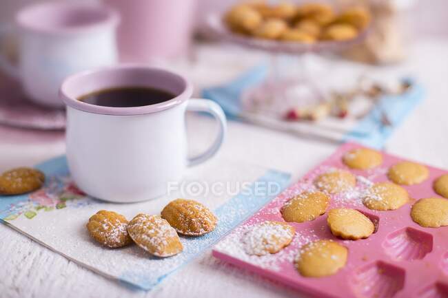 Madeleines francesas em uma mesa de madeira branca com decorações azuis e rosa e uma xícara de café — Fotografia de Stock