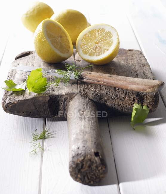 Halbierte Zitronen auf einem alten Holzbrett mit Petersilie, Dill und einem Messer — Stockfoto