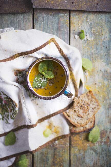 Морковь сливочный суп в эмали кружку; украшен свежей мяты и морской соли хлопья — стоковое фото