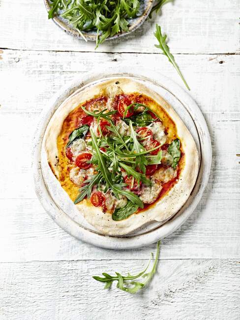 Pizza de corteza fina con espinacas, salami y gorgonzola rematada con rúcula fresca - foto de stock