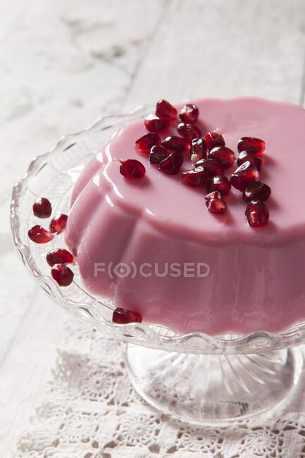 Розовое молочное желе, покрытое семенами граната на подставке для торта и старинной кружевной скатертью — стоковое фото