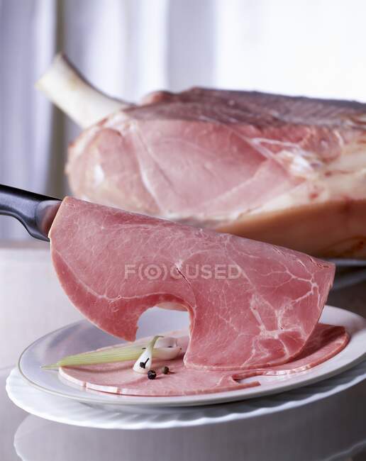 Um pedaço de presunto com uma faca e presunto fatiado em um prato — Fotografia de Stock