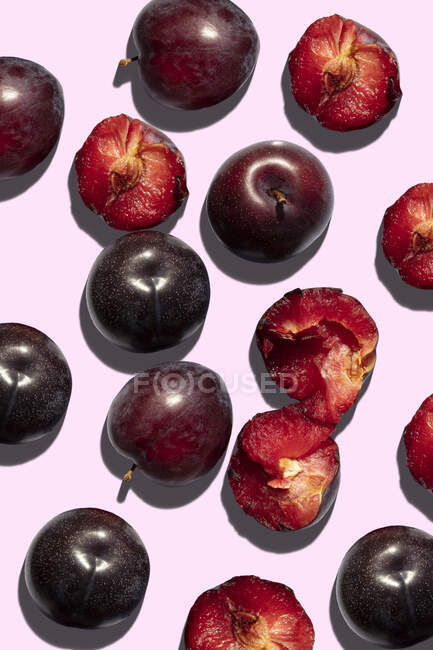 Prunes fraîches, entières et coupées en deux sur fond rose — Photo de stock