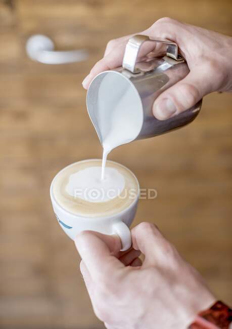 Un barista versant du lait moussé dans une tasse de cappuccino — Photo de stock