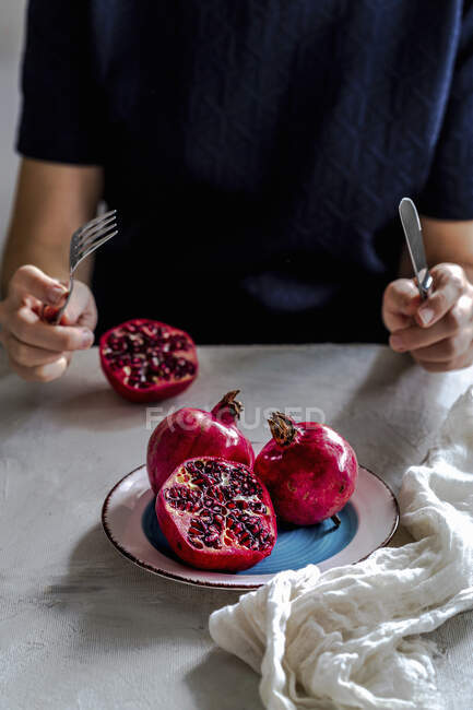 Woman holding pomegranate seeds and knife on a wooden table — Stock Photo