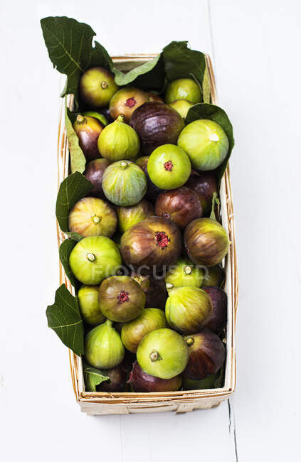 Recipiente de madera lleno de higos verdes y morados frescos con hojas - foto de stock