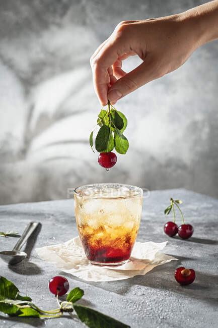 Iced cherry mocktail with hand holding cherry — Stock Photo