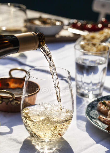 Weißwein wird in ein Glas gegossen, auf einem Tisch im Freien mit Pasta cacio e pepe, Käse und Pfeffer, Basilikum und Garnelenspießen — Stockfoto