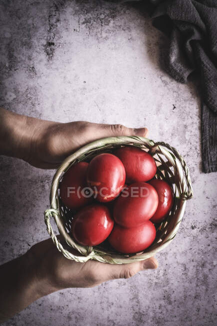 Hands holding basket with red eggs — Stock Photo