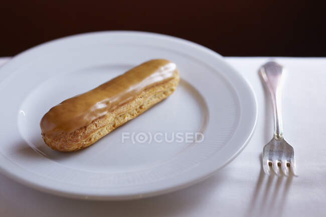 Caramel-glazed eclair on white plate — Stock Photo