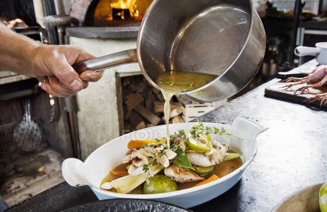 Scena della cucina: una persona che versa brodo sul cibo in un piatto di porcellana — Foto stock