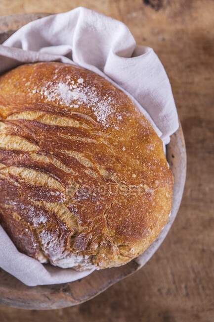 Wheat bread loaf with flour on cloth and wooden surface — Stock Photo
