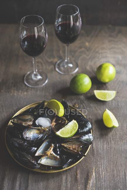 Moules cuites servies avec des quartiers de citron vert et du vin rouge — Photo de stock