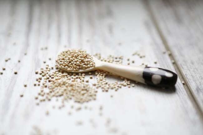 Quinoa sur une cuillère et un fond en bois blanc — Photo de stock