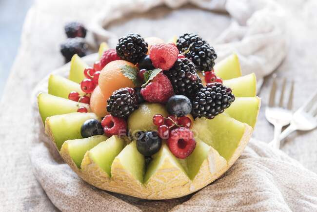 Eine halbierte Melone gefüllt mit Melonenbällchen und frischen Beeren — Stockfoto