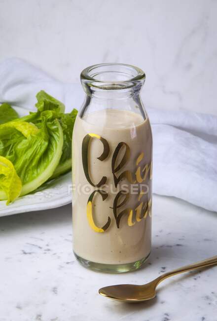 A bottle of caesar salad dressing with romaine lettuce in backround. — Stock Photo