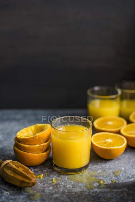 Vasos de zumo de naranja exprimido fresco con mitades de frutas y cáscaras - foto de stock