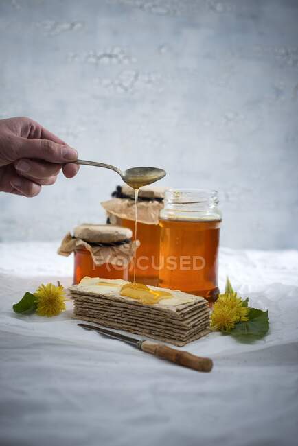 La mano de una mujer rociando jarabe de diente de león sobre pan crujiente - foto de stock