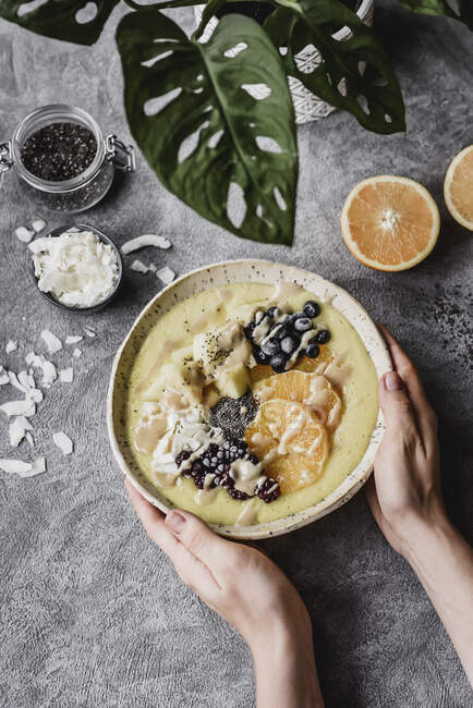 Hands holding bowl with pineapple, orange, chia, blackberries, blueberries and coconut flakes — Stock Photo