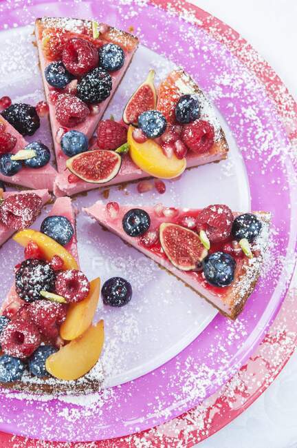 Overhead view of strawberry cheesecake slices on three pink and red plates topped with fresh fruit and raspberry coulis — Stock Photo