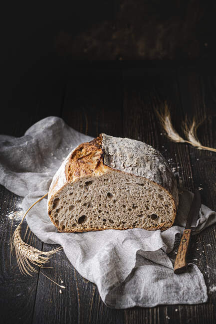 Metà del pane Sourdough su stoffa con spikelets e coltello — Foto stock