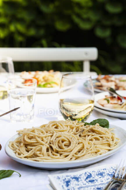 Bandeja de cacio e pepe, pasta con queso y pimienta con albahaca, y pinchos de camarones en la mesa al aire libre - foto de stock