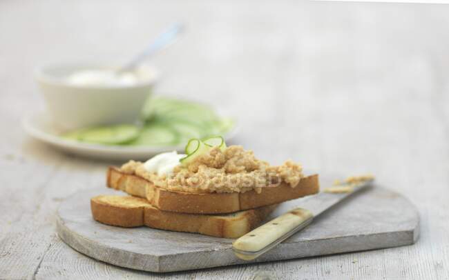 Salmon pate and cucumber slice on toasts with knife on board — Stock Photo
