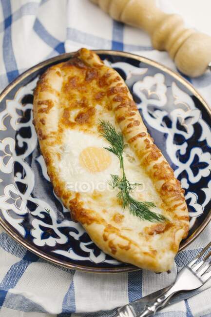 Uma pizza de pão achatado em forma oval com um ovo frito no topo — Fotografia de Stock