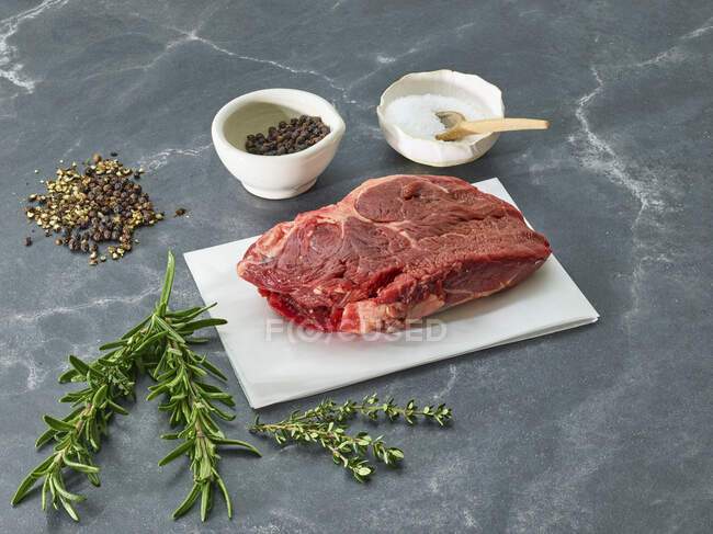 Raw sirloin steak on a piece of paper surrounded by herbs and spices — Stock Photo