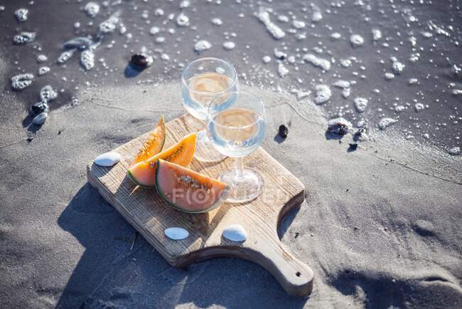 Two glasses of white wine and cantaloupe melon on sand beach — Stock Photo