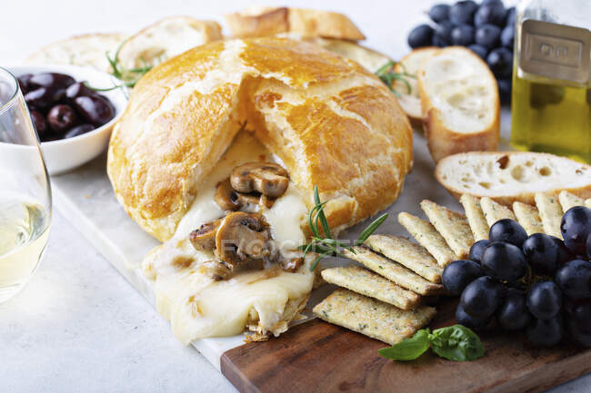 Baked brie wrapped in puff pastry with mushrooms with bread and cracker on a board — Stock Photo