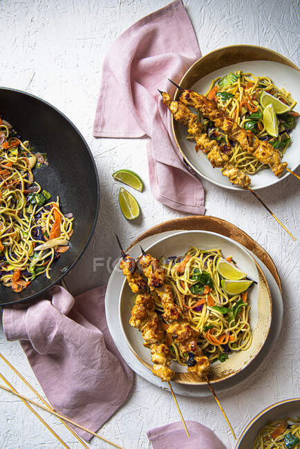 Chicken satay skewers with stir fry vegetable noodles and lime wedges — Stock Photo