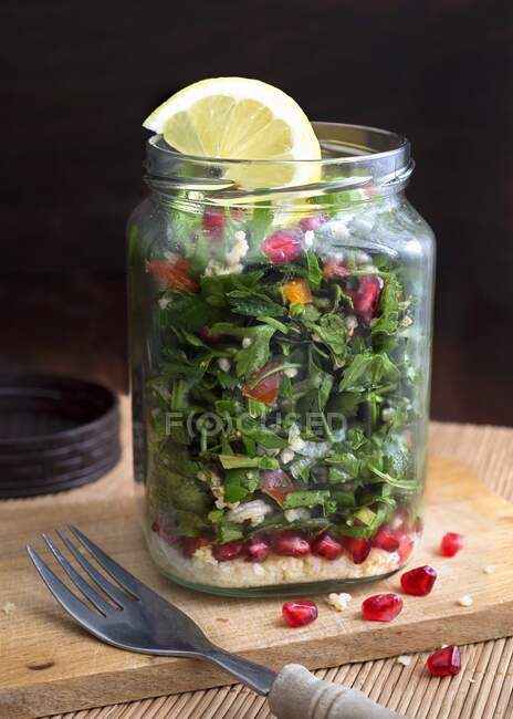 Millet taboule in a glass jar with pomegranate seeds, parsley and mint — Stock Photo