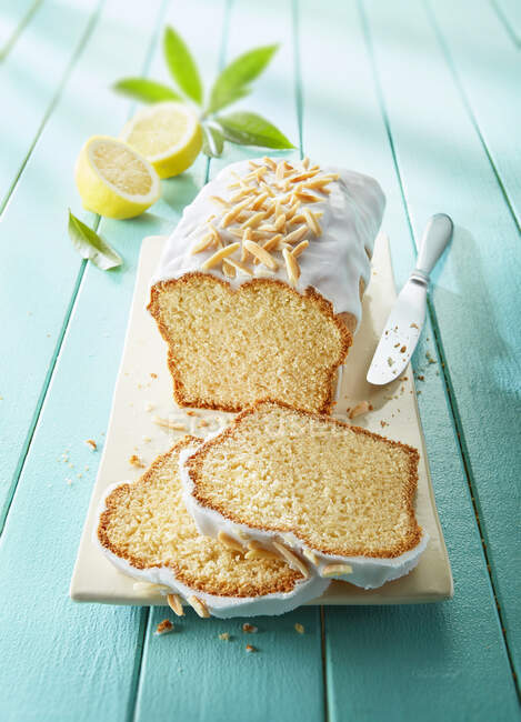 Lemon cake with icing and almond nibs, sliced — Stock Photo