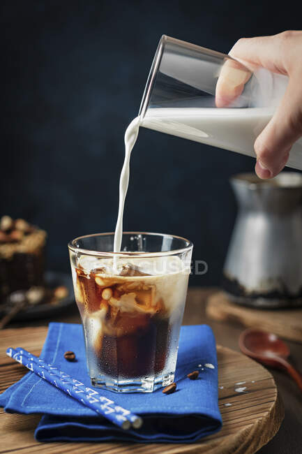 Eiskalter Kaffee mit einer Hand, die Milch einschenkt — Stockfoto