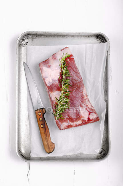 Piece of pork belly with a sprig of rosemary in an metal roasting tray — Stock Photo