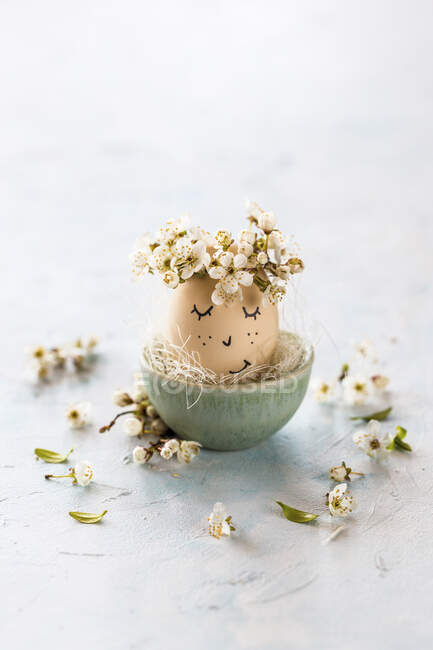 Un uovo di Pasqua con un viso e petali di fiore — Foto stock