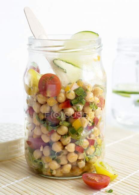 Un'insalata di ceci in un vaso di vetro con pomodori, peperoni, cipolle rosse, cipollotti, spezie, lime, olio d'oliva e prezzemolo fresco — Foto stock