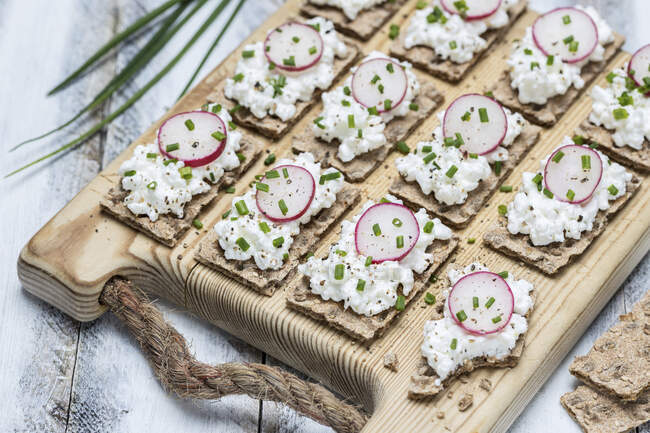 Slices of crispbread with cottage cheese and radishes on a wooden board — Stock Photo