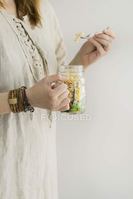Eine Frau im Leinenkleid hält ein Salatglas mit Vollkornnudeln, Karotten, Blumenkohl und grünen Salatblättern in der Hand — Stockfoto