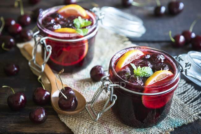 Jam with cherries, lemon slices and mint in glass jars — Stock Photo
