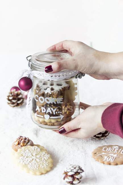 Hands holding a glass jar with decorated Christmas cookies — Stock Photo