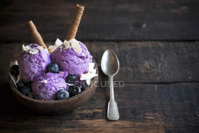 Scoops of blueberry ice cream topped with flaked almonds and chocolate wafer rolls in a wooden bowl — Stock Photo