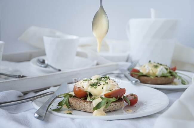 Eggs benedict with hollandaise sauce, rocket, and tomatoes on toast — Foto stock