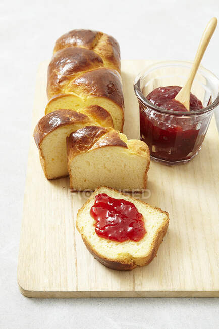 Plaited bread with strawberry jam in jar with spoon and on slice — Stock Photo