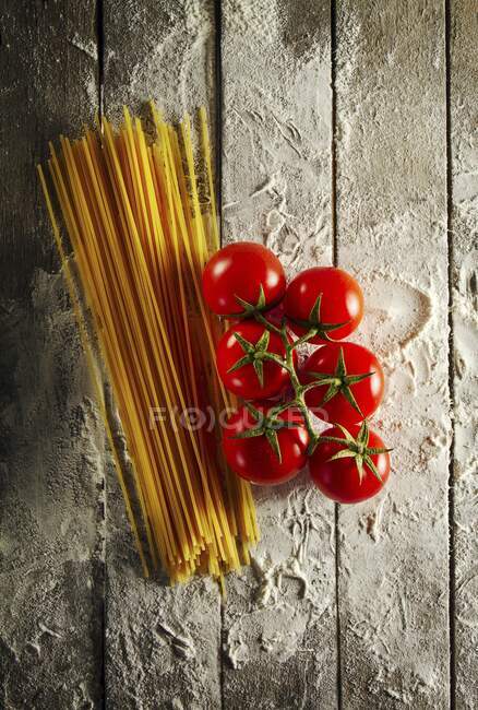 Tomates cereja com espaguete e farinha em uma mesa de madeira — Fotografia de Stock