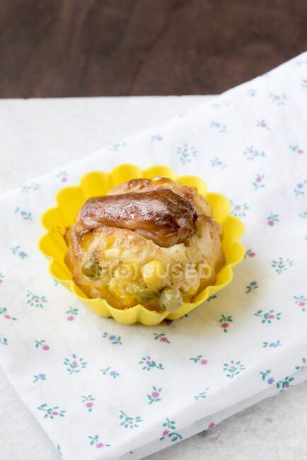 A savoury muffin with a Frankfurter sausage, corn and peas in a yellow muffin case on top of a floral napkin — Stock Photo
