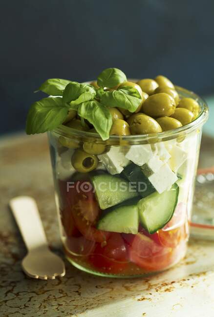 Una ensalada de tomates, pepinos, feta, aceitunas verdes y albahaca en un vaso - foto de stock